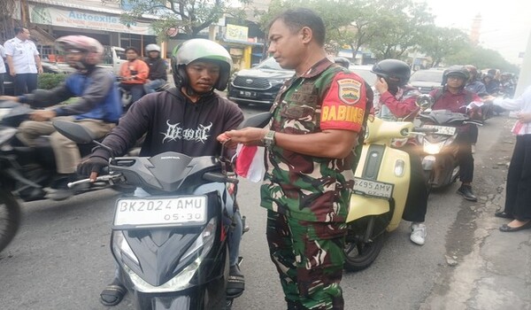 Babinsa Koramil 0201-04/MK Bagikan Bendera Merah Putih kepada Pengendara Motor